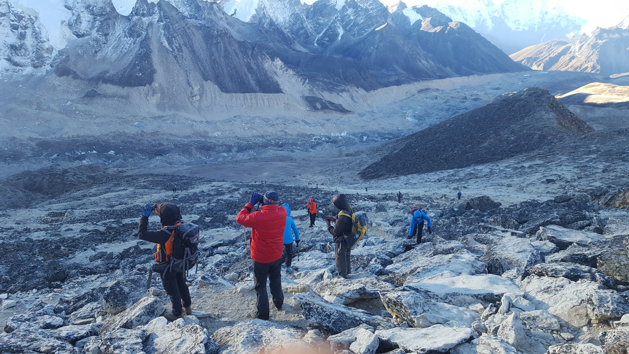 A line of trekkers with backpacks climbing a rocky mountain trail in the Khumbu